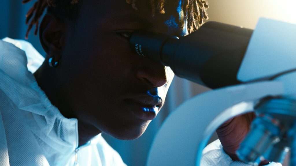 A focused scientist in a lab coat examining samples through a microscope.